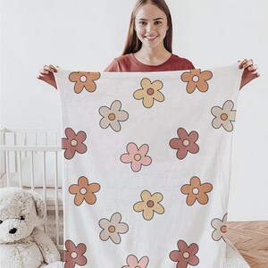 K&ouml;nnte beinhalten: Eine wei&szlig;e Babydecke mit einem Blumenmuster mit orangefarbenen, gelben und rosa Blumen. Die Decke ist weich und flauschig, perfekt zum Kuscheln.