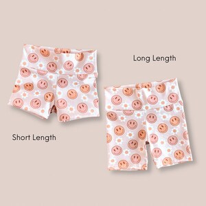 May include: Two pairs of pink shorts with a white smiley face and daisy print. The shorts are shown in two lengths, short and long.