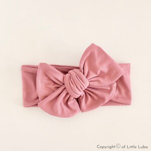 May include: A dusty rose knotted headband with a large bow. The headband is made of soft, stretchy fabric.