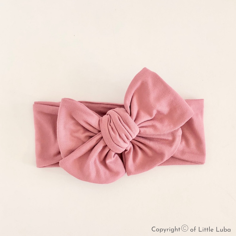 May include: A dusty rose knotted headband with a large bow. The headband is made of soft, stretchy fabric.