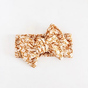 May include: A mustard yellow headband with a white floral pattern tied into a bow.