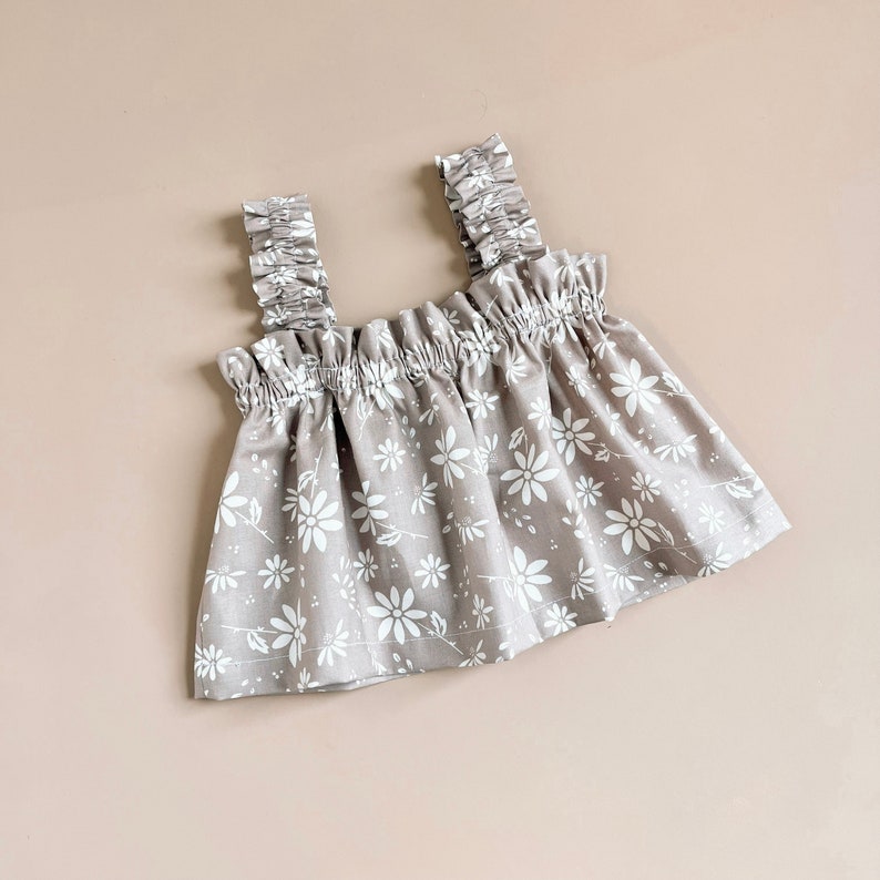 Puede incluir: Una blusa gris sin mangas con estampado floral blanco y tirantes con volantes.