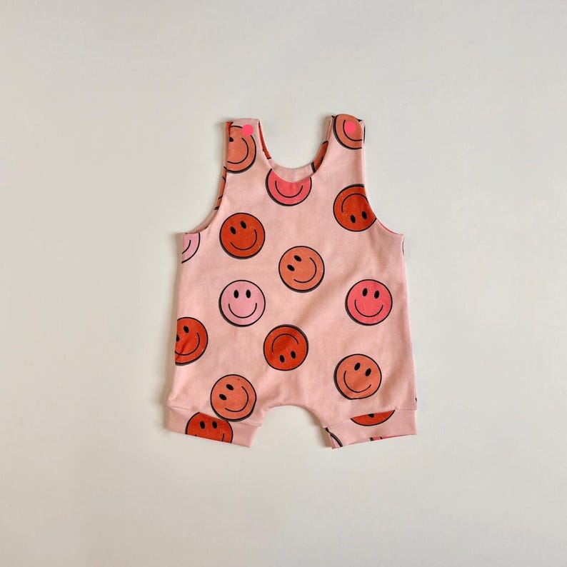 May include: Pink baby romper with a pattern of red, orange, and pink smiley faces.