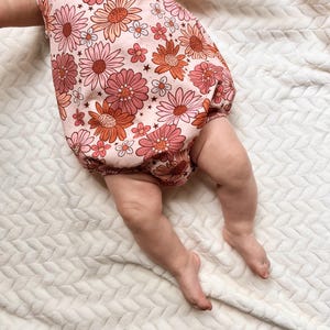 Op de afbeelding: Een baby die een roze en oranje bloemenprint onesie draagt met een sterrenpatroon. De onesie heeft een gerimpelde onderkant en is gemaakt van een zachte, comfortabele stof.