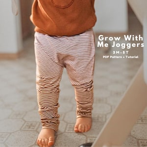 Puede incluir: Un niño lleva un pantalón de chándal a rayas marrones y blancas y una camisa de manga larga marrón. El texto de la derecha dice "Grow With Me Joggers" y "3M-5T PDF Pattern + Tutorial".
