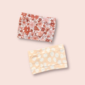 May include: Two fabric headbands, one with a floral pattern in shades of pink and orange on a white background, and the other with a white polka dot pattern on a peach background.