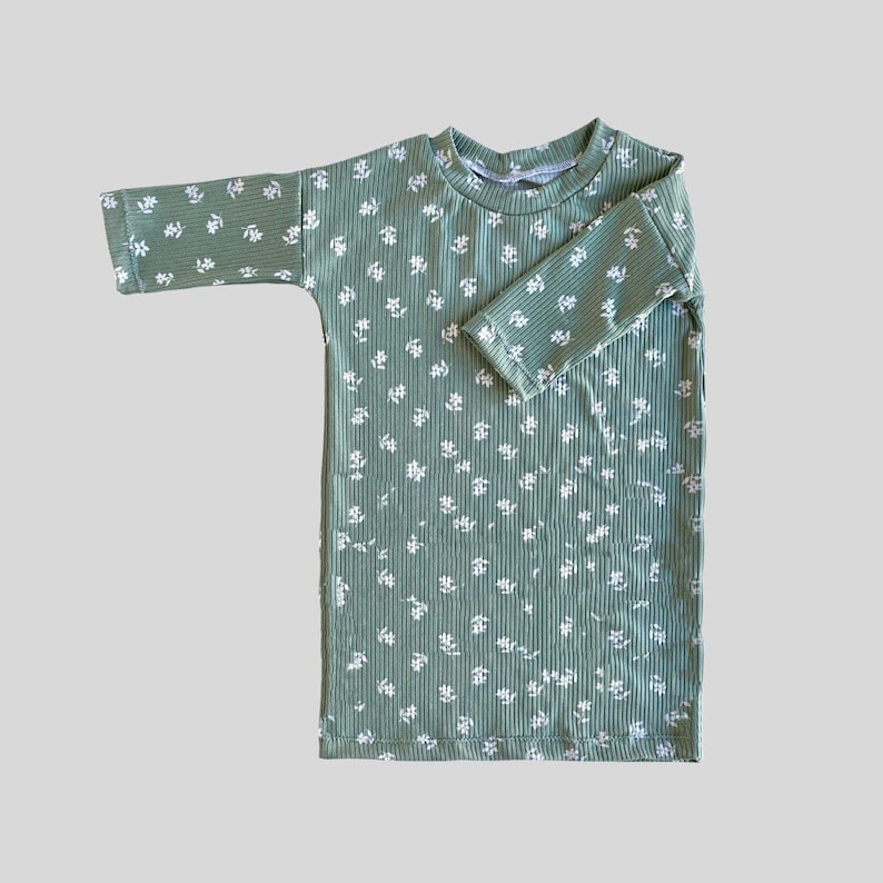 K&ouml;nnte beinhalten: Ein gr&uuml;nes, lang&auml;rmliges Kleid mit wei&szlig;em Blumenmuster. Das Kleid hat eine gerippte Textur und einen runden Ausschnitt.
