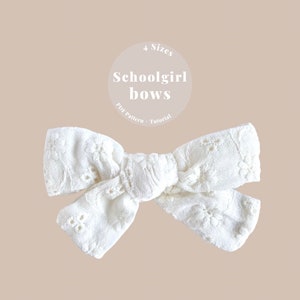 May include: White fabric bow with a floral pattern. The bow is tied in a knot and has a slightly ruffled edge. The text "Schoolgirl bows" is written in white on a circle with a white background. The text "PDF Pattern + Tutorial" is written in white on a circle with a white background. The text "4 Sizes" is written in white on a circle with a white background.
