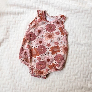 Op de afbeelding: Een roze baby romper met een bloemenprint met roze, oranje en witte bloemen. De romper is mouwloos en heeft een ronde hals.
