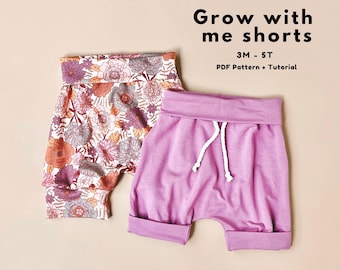 May include: Two pairs of baby shorts. One pair features a floral pattern in shades of orange, purple, and white. The other pair is solid lavender with a white drawstring. Text on the image reads "Grow with me shorts" and "3M - 5T".