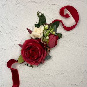 Op de afbeelding: Een rood fluwelen lint gebonden om een ​​boeket rode en witte rozen met groene bladeren.