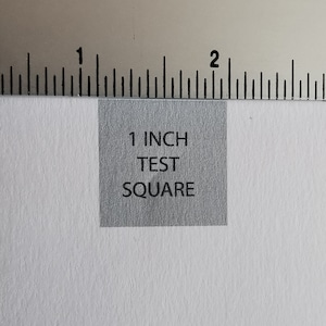 Op de afbeelding: Een grijs vierkant met de tekst "1 INCH TEST SQUARE" erop gedrukt.