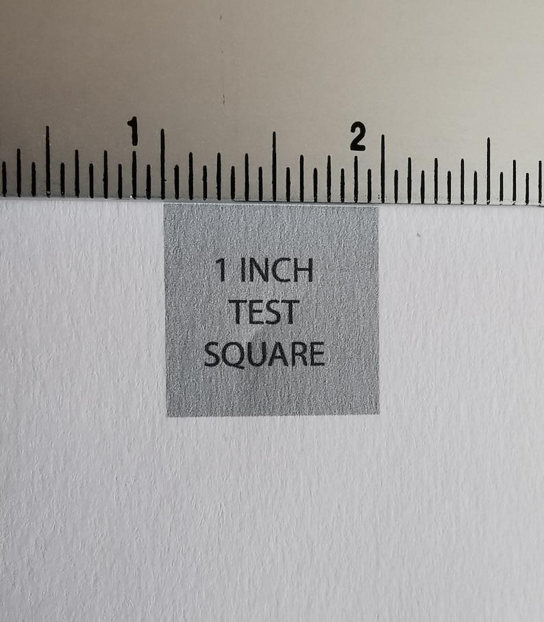 Op de afbeelding: Een grijs vierkant met de tekst "1 INCH TEST SQUARE" erop gedrukt.
