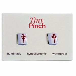 May include: Mahjong tile stud earrings on a white card. The earrings are white with a red Chinese character. The card has the text "Tiny Pinch", "handmade", "hypoallergenic", and "waterproof".