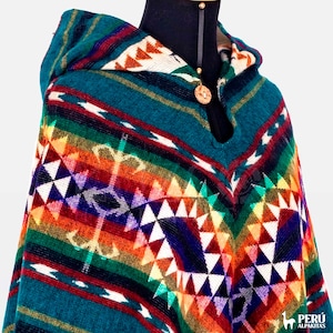 May include: A teal blue hooded poncho with a colorful geometric pattern. The poncho is made of alpaca wool and features a wooden button closure.