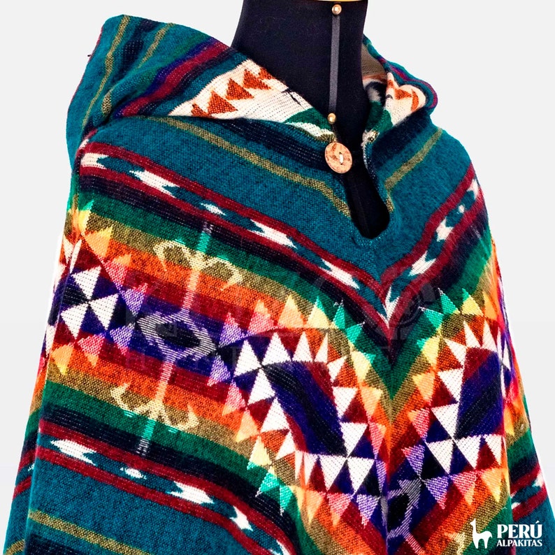 May include: A teal blue hooded poncho with a colorful geometric pattern. The poncho is made of alpaca wool and features a wooden button closure.