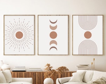 May include: Three framed wall art prints with a minimalist design. The prints feature a sunburst, phases of the moon, and arched lines with a central circle, all in shades of brown and beige. The frames are a light brown color.