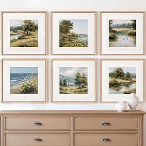Puede incluir: Seis impresiones artísticas de paisajes enmarcadas con marcos de madera neutros se exhiben sobre una cómoda beige. El arte presenta escenas serenas de la naturaleza, incluyendo cuerpos de agua, árboles y campos, en colores suaves y apagados. Dos jarrones de cerámica blanca están sobre la cómoda.