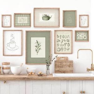 Può includere: Una cucina con un piano di lavoro e armadi bianchi. Ci sono diverse stampe incorniciate sul muro, tra cui una stampa di una teiera, una stampa di una tazza di caffè e una stampa di un orto. Ci sono anche alcune piante sul piano di lavoro.