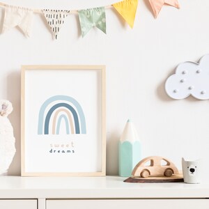 May include: A framed print with a blue and tan rainbow design and the words "sweet dreams". The print is displayed on a white dresser with a plush bear head, a cloud-shaped light, and wooden toys. A colorful banner hangs above.