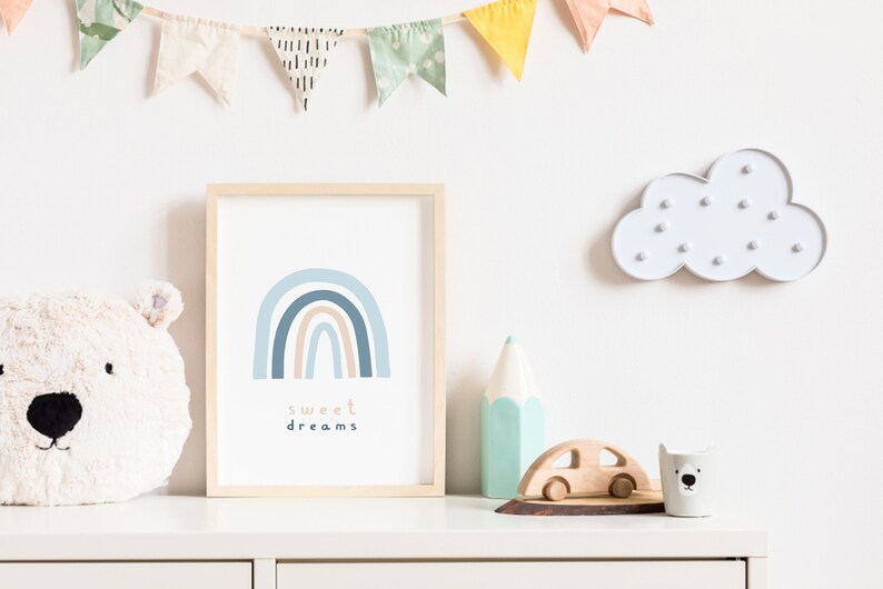 May include: A framed print with a blue and tan rainbow design and the words "sweet dreams". The print is displayed on a white dresser with a plush bear head, a cloud-shaped light, and wooden toys. A colorful banner hangs above.