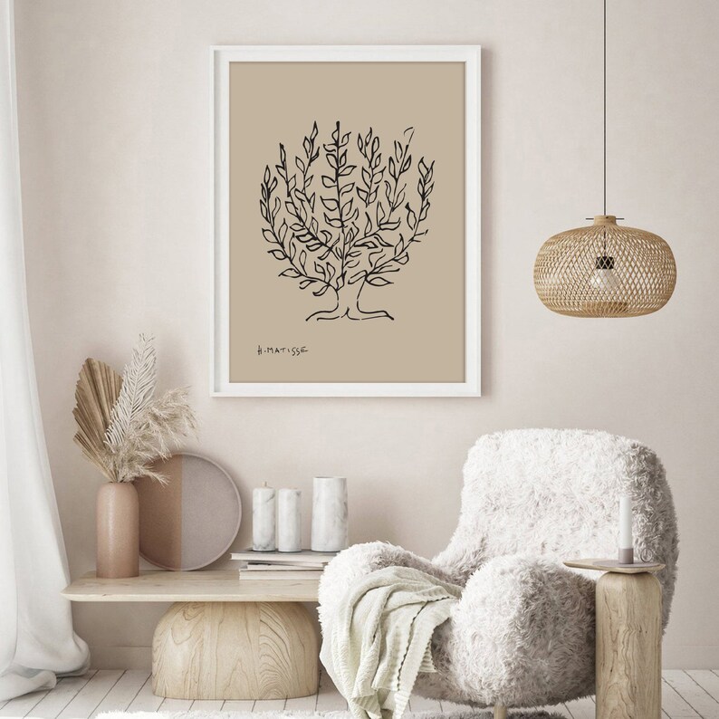 May include: A black and white line drawing of a tree with the signature "H. Matisse" in the bottom left corner. The drawing is framed in a white frame and hangs on a beige wall. A fluffy white armchair sits in front of the artwork.