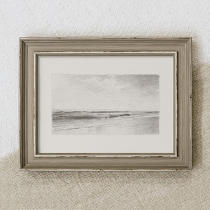 May include: A framed black and white pencil drawing of a seascape. The drawing depicts a calm ocean with a sandy beach in the foreground and a cloudy sky in the background.