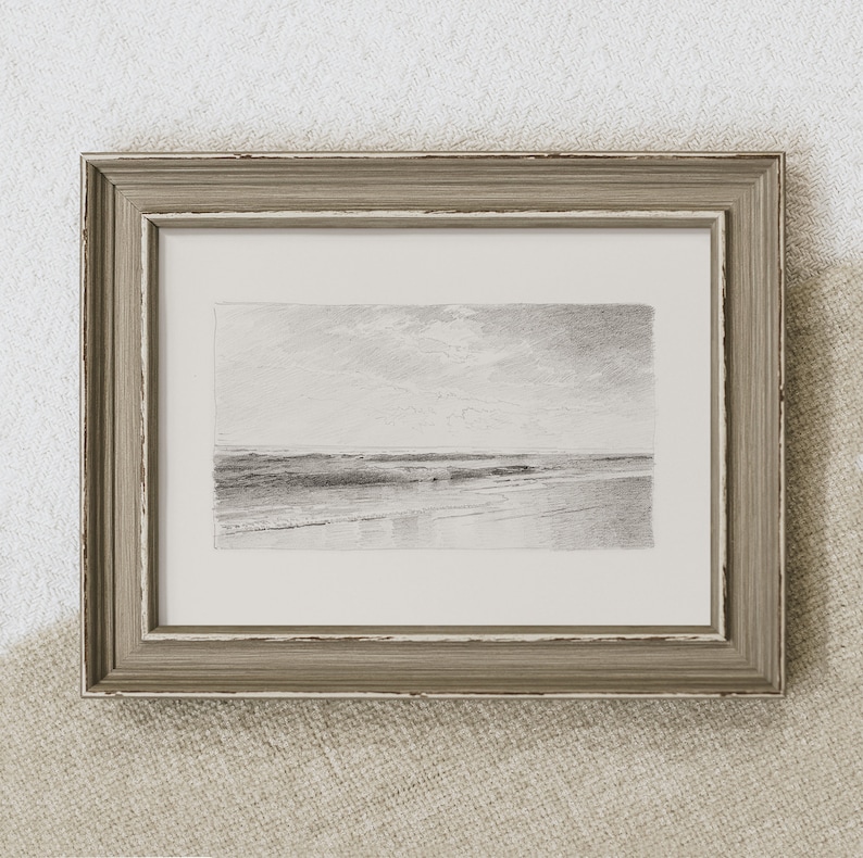 May include: A framed black and white pencil drawing of a seascape. The drawing depicts a calm ocean with a sandy beach in the foreground and a cloudy sky in the background.