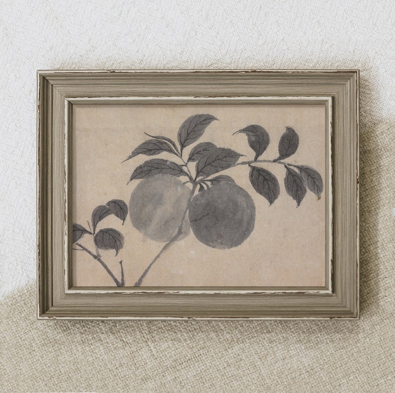 May include: A framed artwork featuring a monochrome ink wash painting of two fruits on a branch with leaves. The artwork is in a rectangular frame with a distressed, light gray finish. The background is a neutral beige.