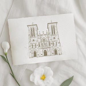 May include: A sepia-toned sketch of a cathedral with two bell towers and a detailed facade. The artwork is on textured paper, with a white flower and stem in the foreground. The overall aesthetic is elegant and artistic.