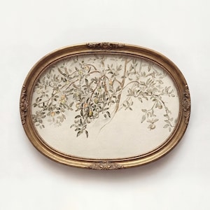 Może przedstawiać: Owalne, oprawione dzieło sztuki w kolorze antycznego złota. Dzieło przedstawia drzewo z zielonymi liśćmi i żółtymi owocami. Rama ma ozdobne detale. Tło jest w jasnobeżowym kolorze.