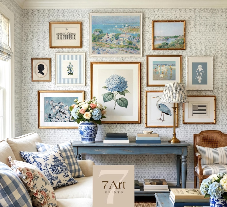 May include: A gallery wall featuring framed art prints with gold frames. The prints depict landscapes, botanical illustrations, and silhouettes. A blue and white floral vase holds a bouquet of flowers, and a blue console table is below the art.