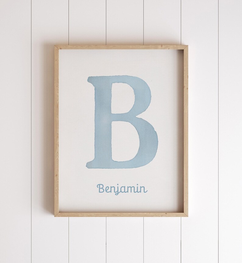 May include: A framed print with a light blue watercolour letter 'B' on a white background. The name 'Benjamin' is written in a matching blue font below the letter. The frame is made of light-coloured wood.