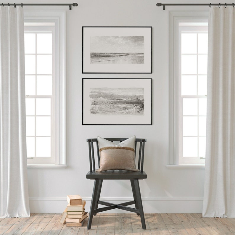 May include: Two black framed prints of seascapes hang on a white wall above a black wooden chair with a beige and brown pillow. The chair is in front of a stack of books.