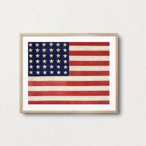 May include: A framed print of a vintage American flag with 48 stars. The flag is faded and worn, giving it a rustic look. The frame is made of natural wood.