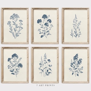 May include: Set of seven framed art prints featuring botanical illustrations in shades of blue. Each print showcases a different floral arrangement against a cream-colored background. The frames are made of light-colored wood. The text "7 ART PRINTS" is at the bottom.