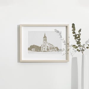 May include: A framed print featuring a detailed sketch of a church with a tall steeple. The artwork is in a neutral color palette, set within a light-colored wooden frame. The image is displayed on a white wall, with a vase of greenery to the right.