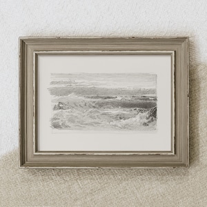 May include: A framed black and white pencil drawing of a seascape. The drawing depicts a rocky coastline with waves crashing against the shore. The frame is a light brown wood with a distressed finish.