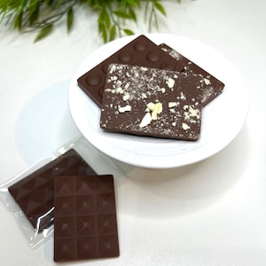 May include: Three chocolate bars on a white plate. Two of the bars are topped with white sprinkles. The third bar is plain.
