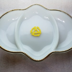 May include: A white ceramic serving dish with a gold rim and three sections. The dish has a scalloped edge and a yellow vinyl record shape in the center.