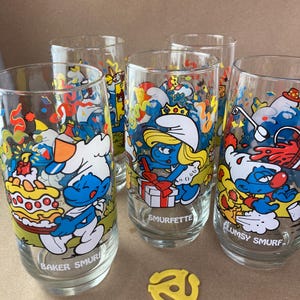 Pu&ograve; includere: Set di quattro bicchieri da bere a tema Puffi. Ogni bicchiere presenta un diverso personaggio dei Puffi con uno sfondo colorato. I bicchieri sono trasparenti e hanno una forma arrotondata. I Puffi sono raffigurati in una scena di festa con coriandoli e palloncini. I bicchieri sono etichettati con i nomi dei Puffi: Puffo Panettiere, Puffetta, Puffo Sbadato.