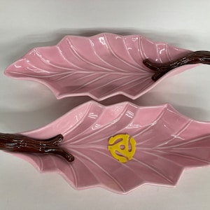 May include: Two pink ceramic leaf-shaped serving dishes with brown twig handles. One dish has a yellow vinyl record design.