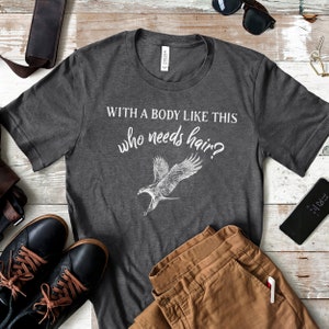 May include: A dark gray t-shirt with a white eagle graphic and the text "With a body like this who needs hair?"