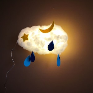 May include: A white cloud-shaped light fixture with a yellow crescent moon and a yellow star. Blue raindrops hang from the bottom of the cloud.