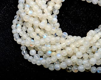 May include: A collection of round, translucent white moonstone beads arranged in a loose, curved formation. Each bead features a smooth, polished surface with subtle internal light reflections and faint blue flashes visible throughout the strand.