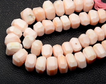May include: A strand of faceted, pale pink, cylindrical beads arranged in a curved line. Each bead features multiple flat, polished surfaces that catch the light, creating a subtle geometric texture along the length of the continuous string.