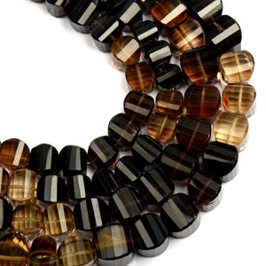 May include: Close-up of a collection of faceted beads in shades of brown and black. Each bead has a striped design in a lighter colour, creating a contrast. The beads are arranged in a curved pattern, showcasing their shape and colour variations.