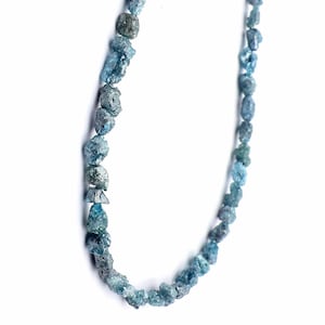 May include: A necklace composed of rough-cut, blue-green gemstones. The stones vary in size and shape, strung together to form a necklace. The background is plain white, highlighting the natural color and texture of the stones.