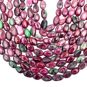 Puede incluir: Una colección de cuentas de rubí zoisita de forma ovalada dispuestas en múltiples hilos. Cada cuenta presenta una superficie pulida con una mezcla de inclusiones minerales en magenta intenso, rojo oscuro y verde vibrante, creando un patrón natural.