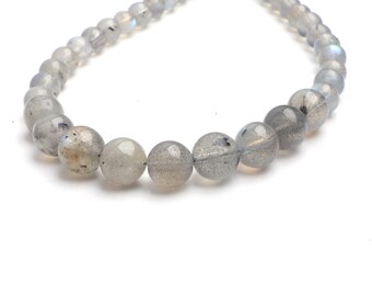 May include: A string of round, grey labradorite gemstone beads. The beads have a speckled appearance and a subtle iridescence. The beads are strung together, creating a necklace or bracelet.